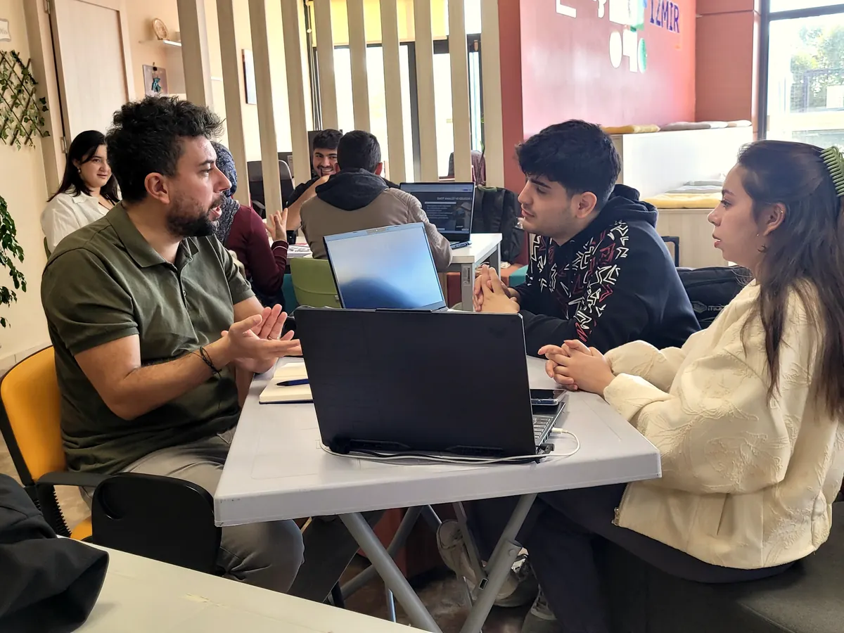 İşletme sahibi mentor iki gence dizüstündeki süreci anlatıyor, açık ofis
